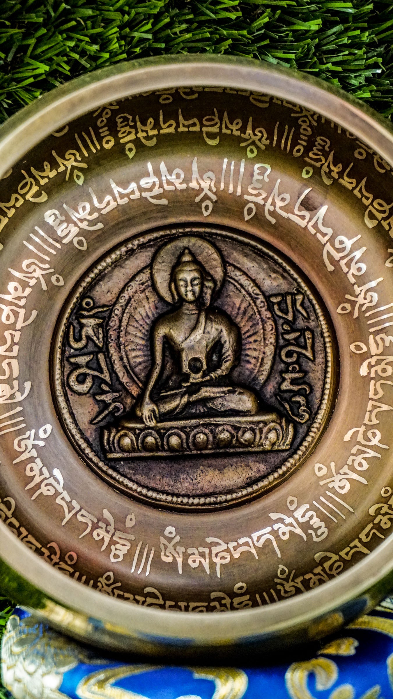 Bronze singing bowl with a carved meditating Buddha at the center, surrounded by the Om Mani Padme Hum mantra inside and engraved again around the outside, radiating peaceful, grounding energy.