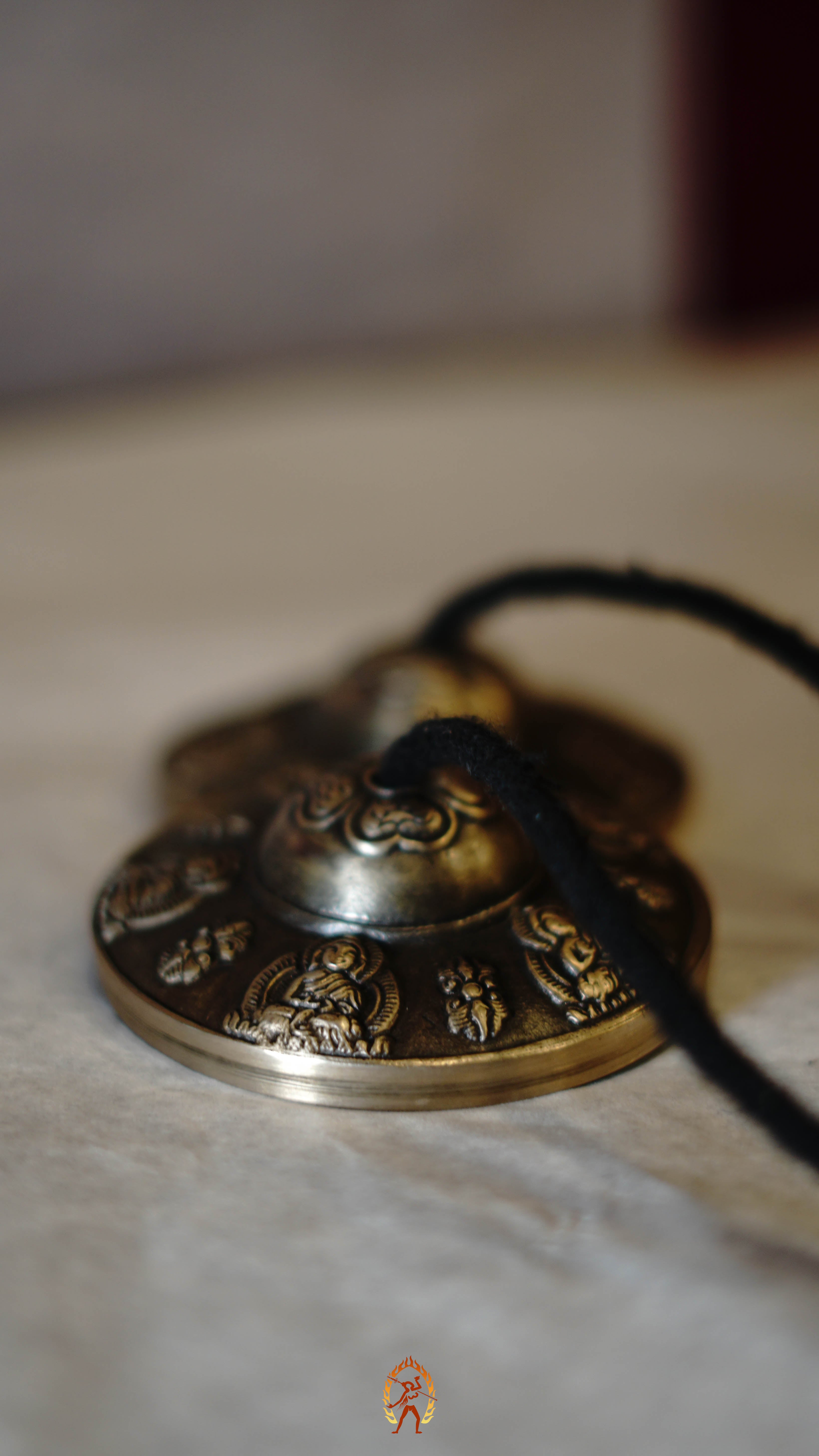 Close-up of bronze tingsha meditation cymbals with detailed Buddhist engravings, resting on a gray textured surface.