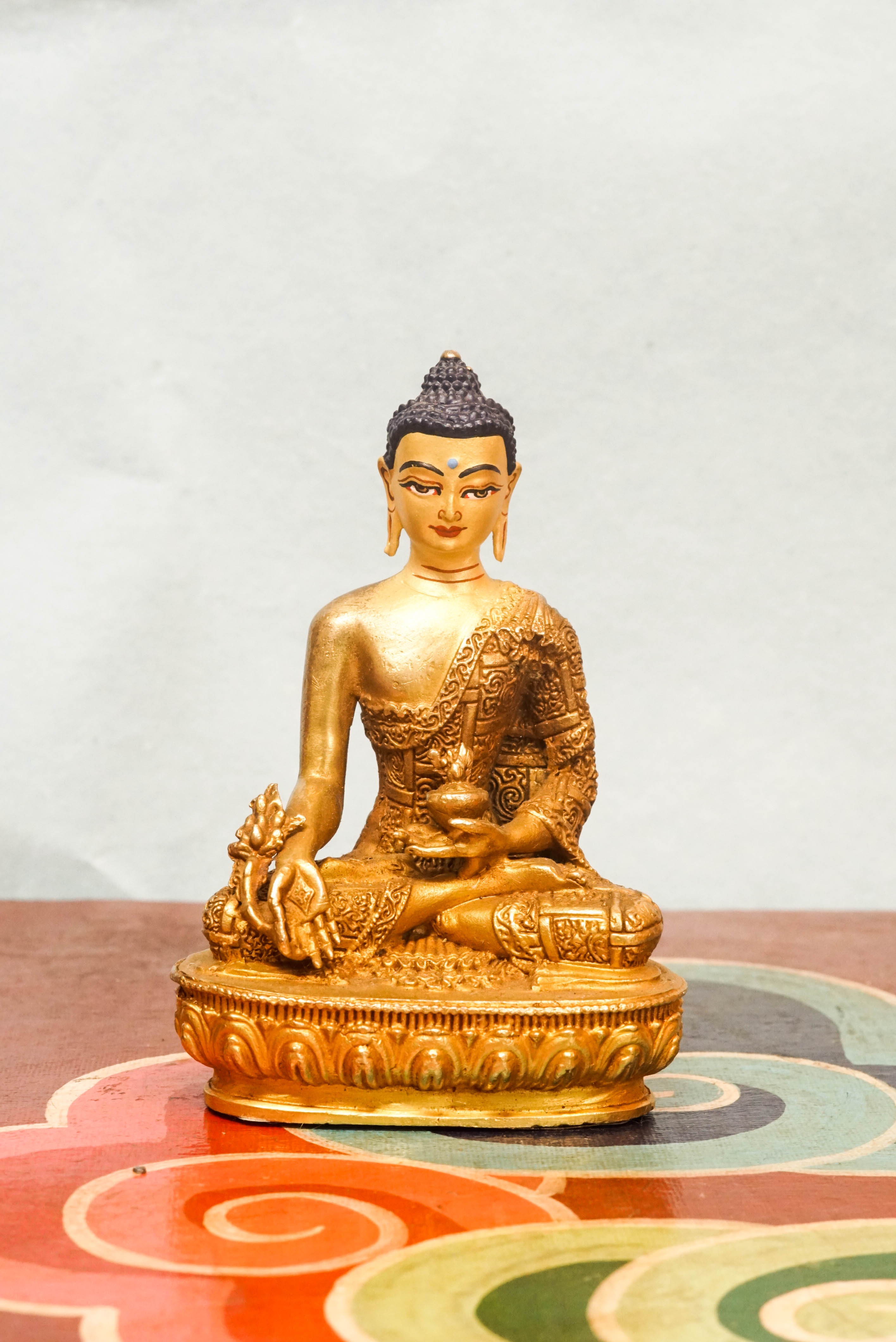 Handcrafted Medicine Buddha statue with open eyes, holding a healing bowl and medicinal plant, surrounded by a radiant lapis blue aura, seated on a lotus pedestal.