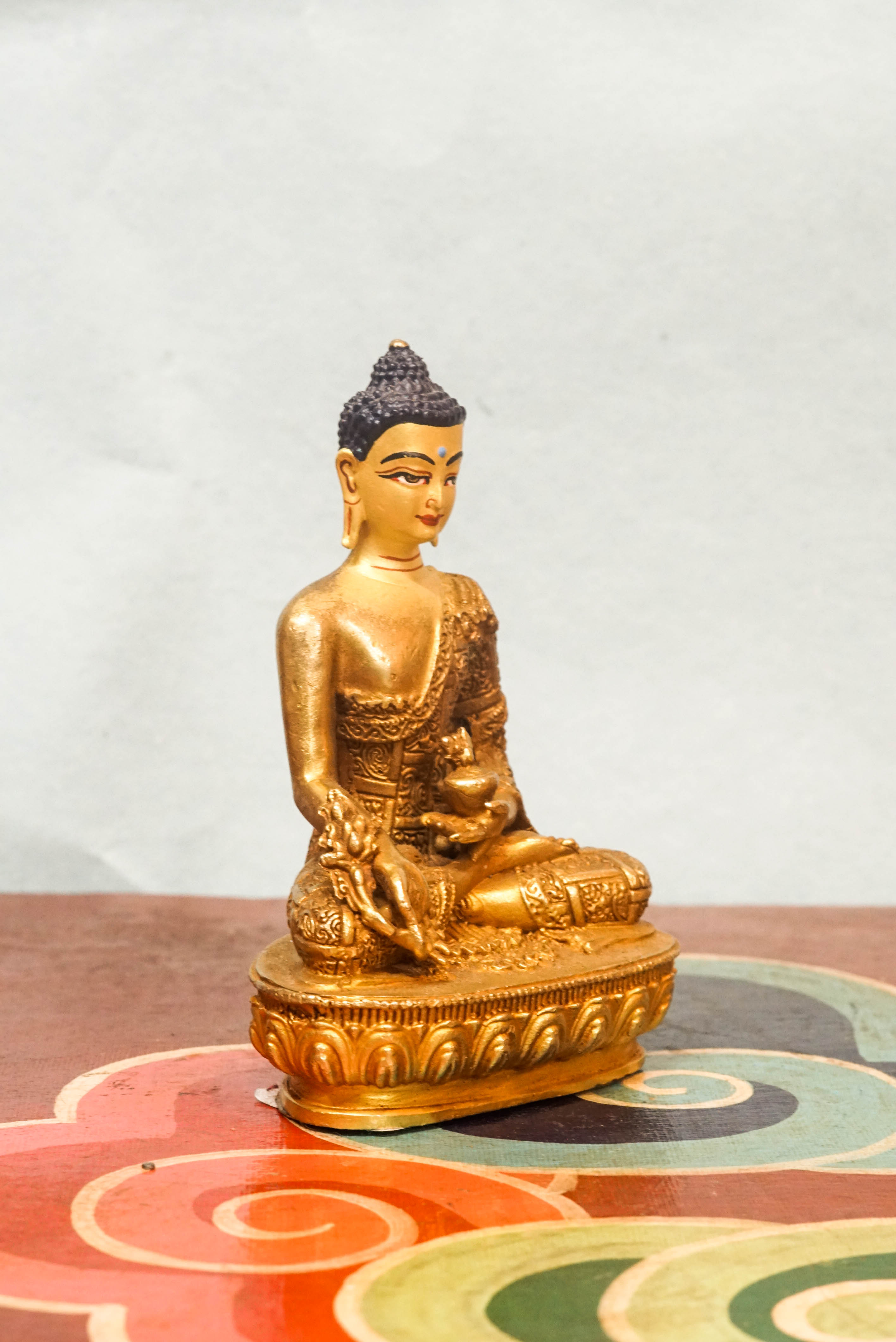 Handcrafted Medicine Buddha statue with open eyes, holding a healing bowl and medicinal plant, surrounded by a radiant lapis blue aura, seated on a lotus pedestal.