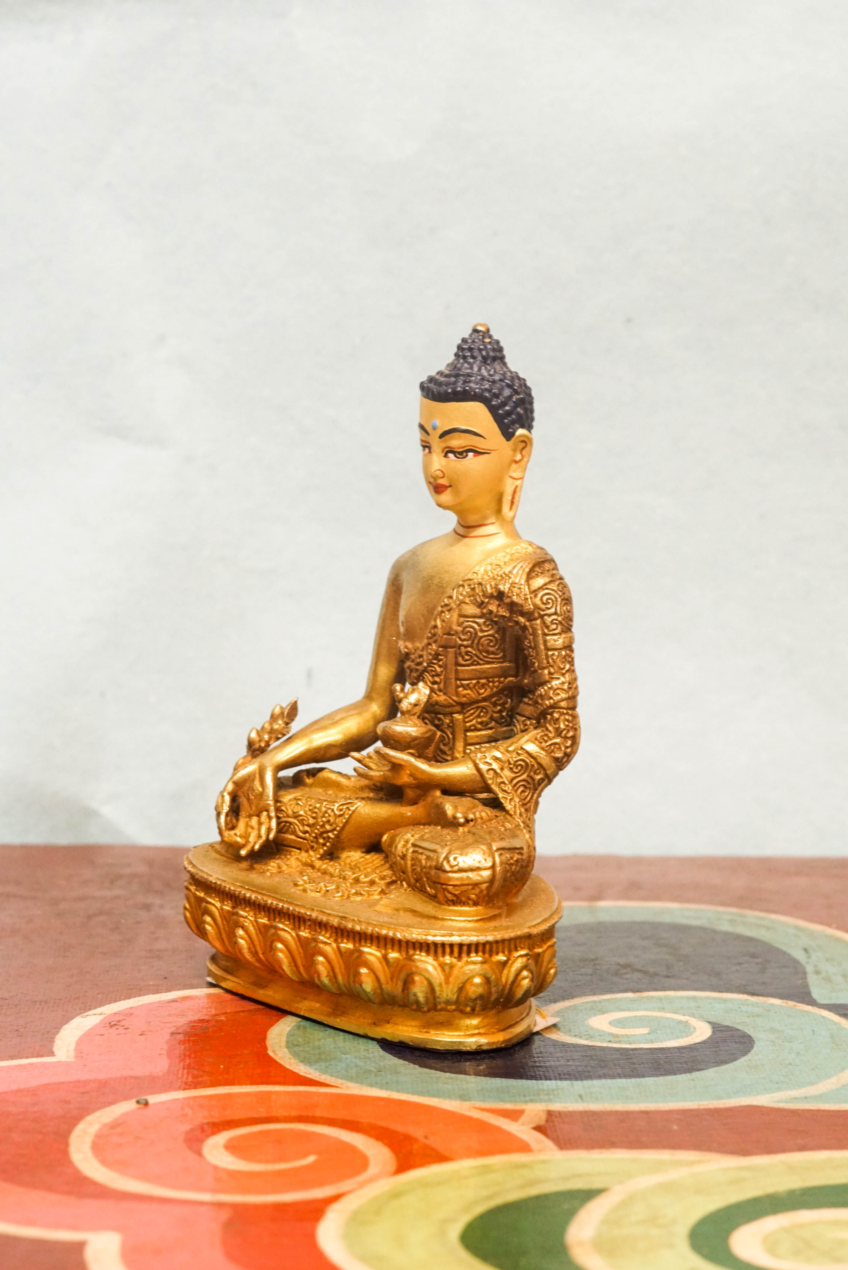 Handcrafted Medicine Buddha statue with open eyes, holding a healing bowl and medicinal plant, surrounded by a radiant lapis blue aura, seated on a lotus pedestal.