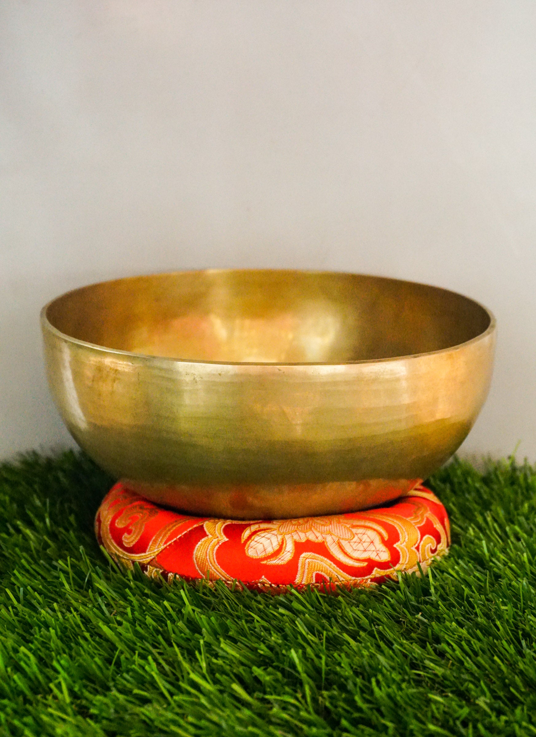 Handmade brass Tibetan singing bowl on a red cushion for sound healing.