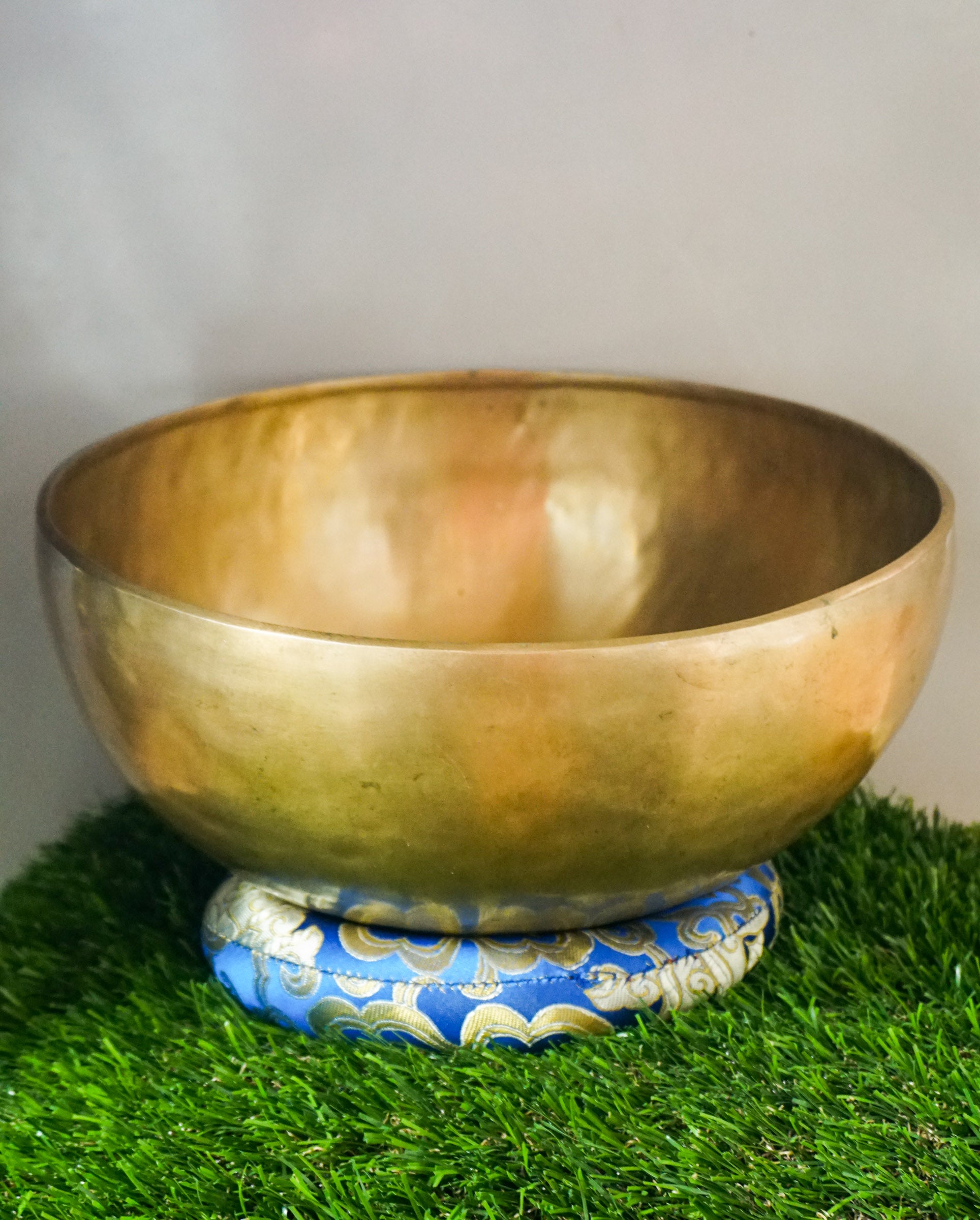 Handmade brass Tibetan singing bowl on a red cushion for sound healing.