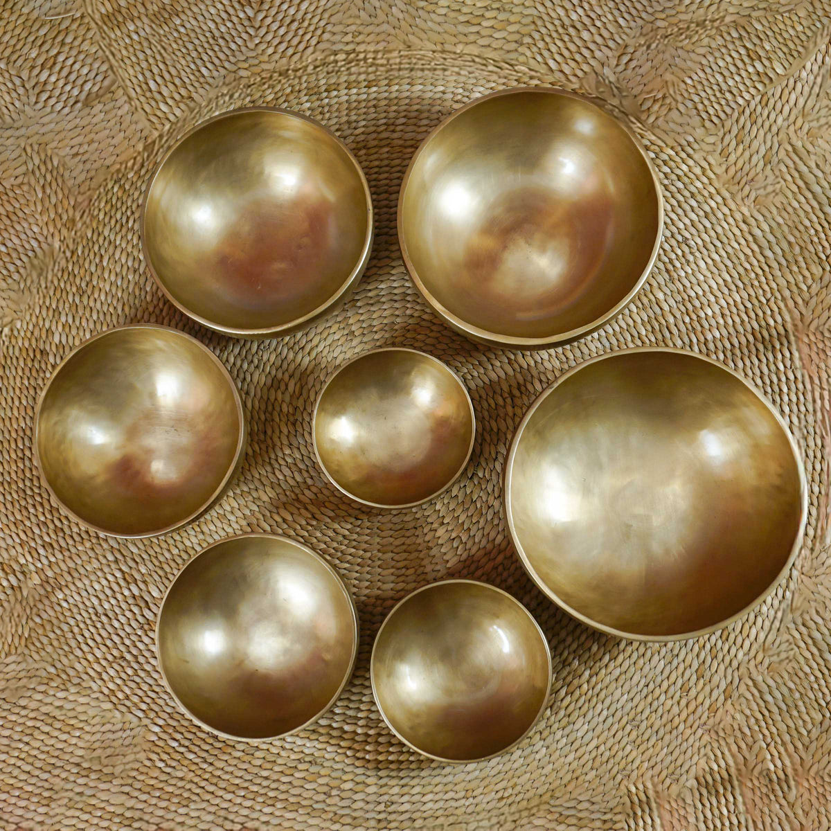 Seven handcrafted Himalayan-style singing bowls arranged in a circular formation, showing graduated sizes and warm antique bronze-gold finishes.