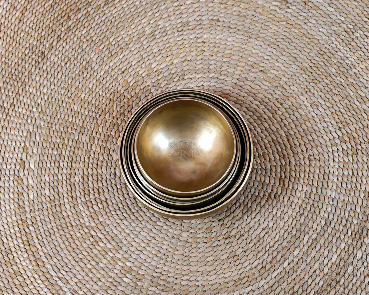 Seven handcrafted Himalayan-style singing bowls arranged in a circular formation, showing graduated sizes and warm antique bronze-gold finishes.