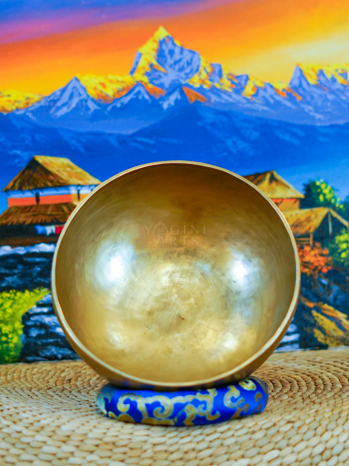 Front view of a handmade bronze-gold singing bowl showing its smooth metal surface and rounded form on a patterned cushion.