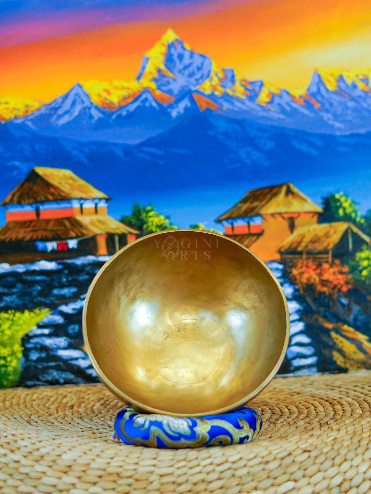 Front view of a handmade bronze-gold singing bowl showing its smooth metal surface and rounded form on a patterned cushion.