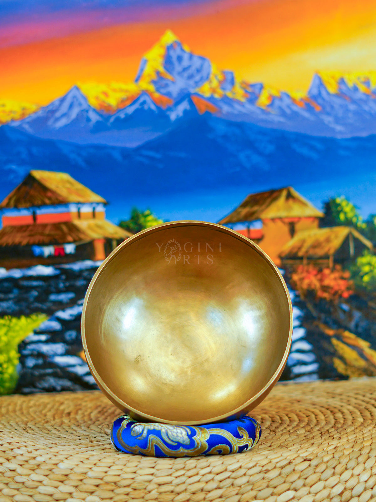 Front view of a handmade bronze-gold singing bowl showing its smooth metal surface and rounded form on a patterned cushion.