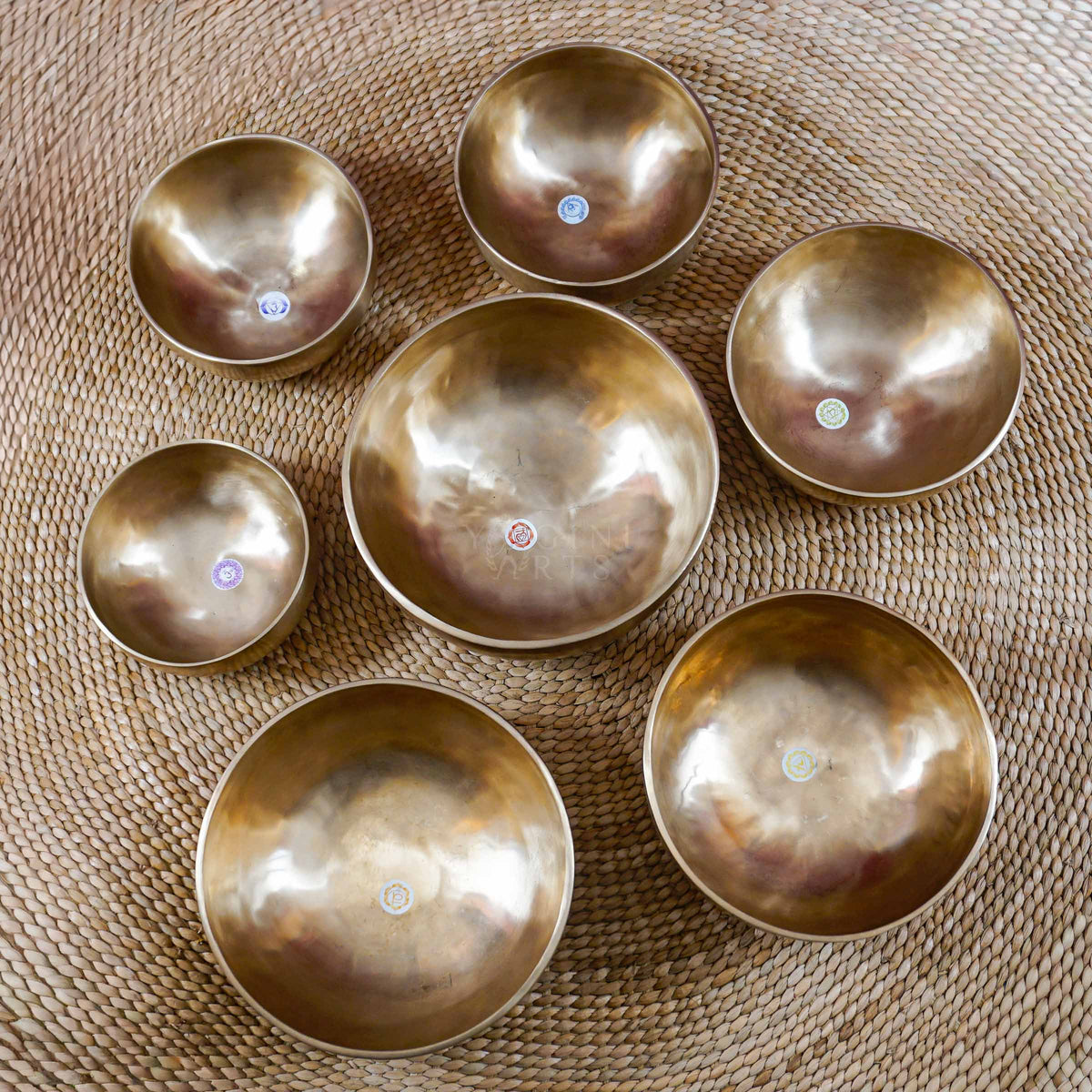 Seven handcrafted singing bowls arranged separately, displaying different sizes and chakra-inspired symbols on their inner surfaces.