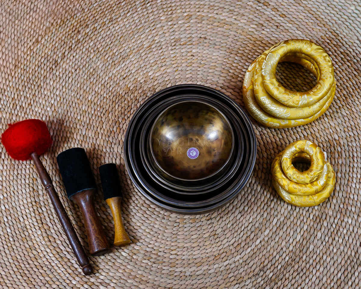 Seven handcrafted chakra singing bowls arranged together, showing different sizes, warm antique metallic finishes and individual chakra symbols.