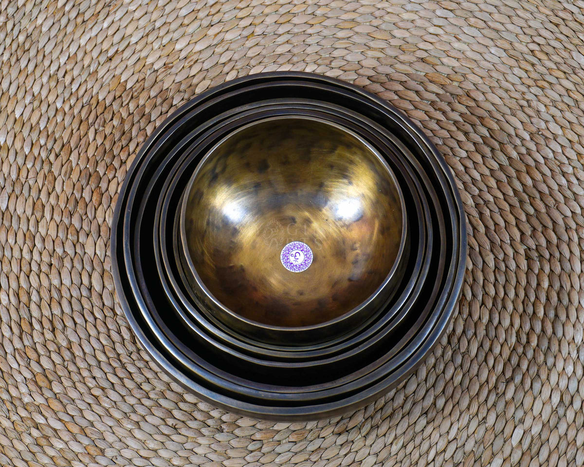 Seven handcrafted chakra singing bowls arranged together, showing different sizes, warm antique metallic finishes and individual chakra symbols.