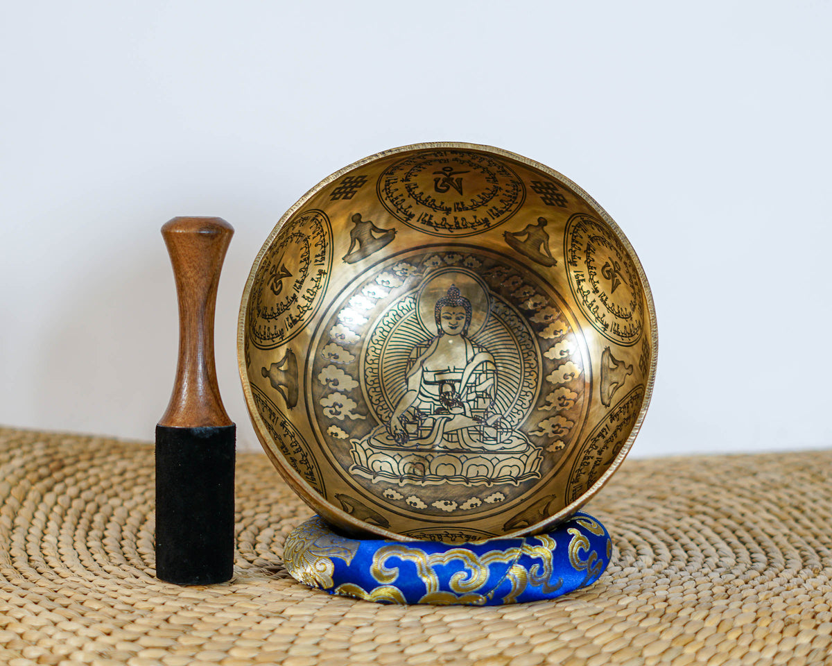 Golden bronze Medicine Buddha singing bowl displayed upright on a blue brocade cushion with a mallet