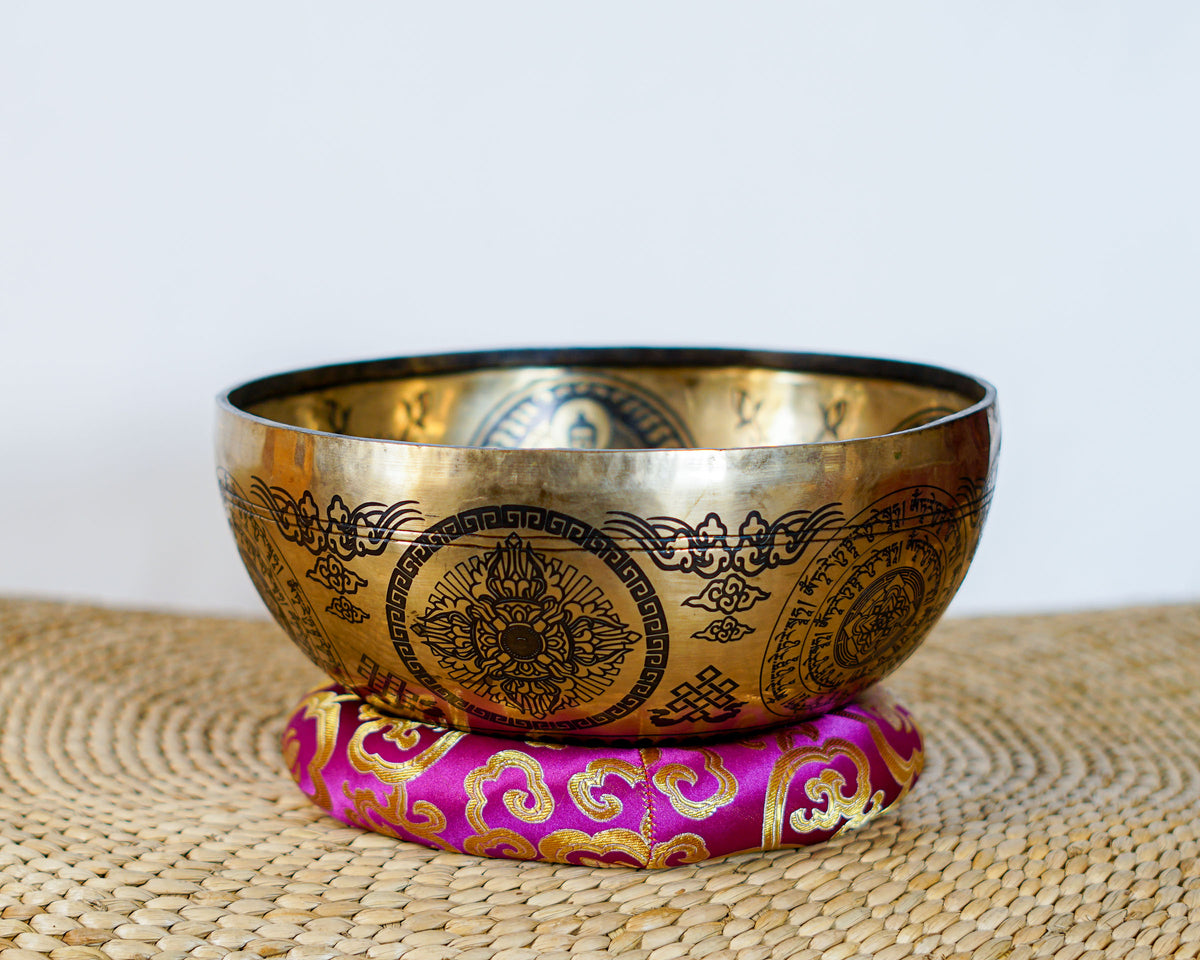 Chengresi singing bowl with Tibetan mantra inscriptions and decorative engravings displayed on a purple brocade cushion