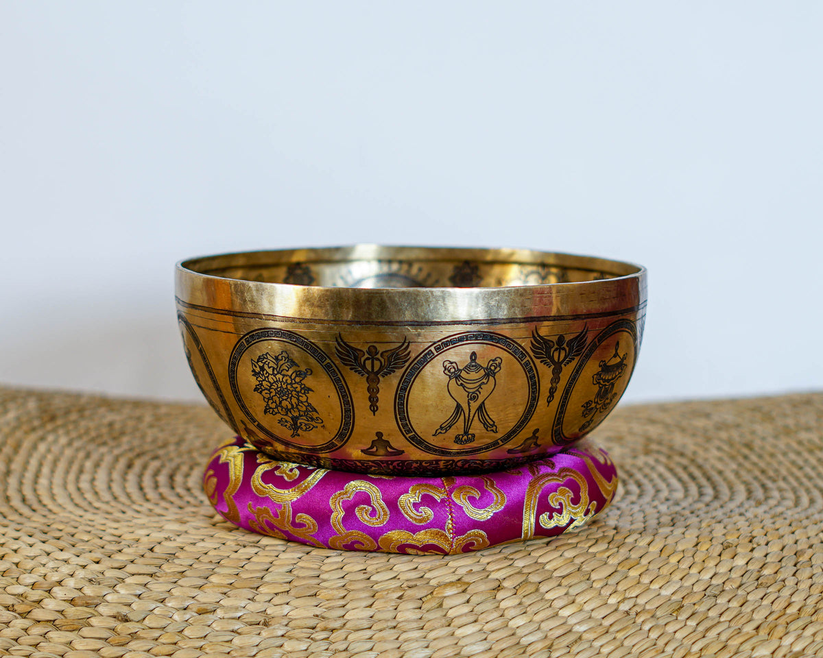 Golden Chakra Yogini singing bowl with engraved exterior motifs displayed on a purple brocade cushion