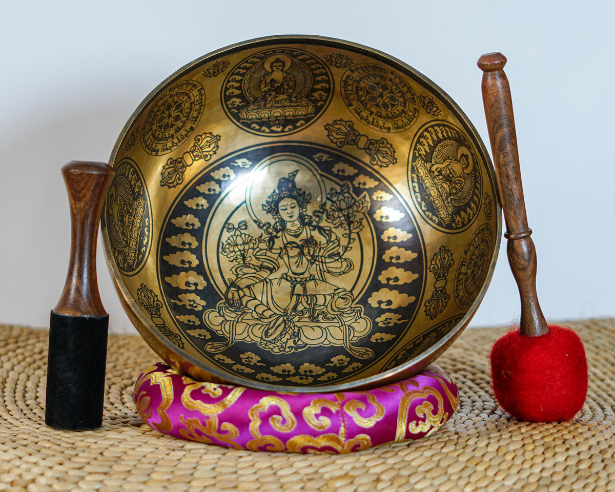 Green Tara bronze singing bowl displayed upright on a purple brocade cushion with two wooden mallets