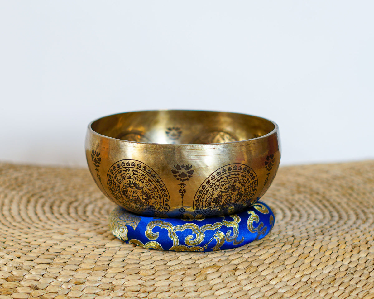 Golden Green Tara singing bowl with intricate exterior engravings displayed on a blue brocade cushion.