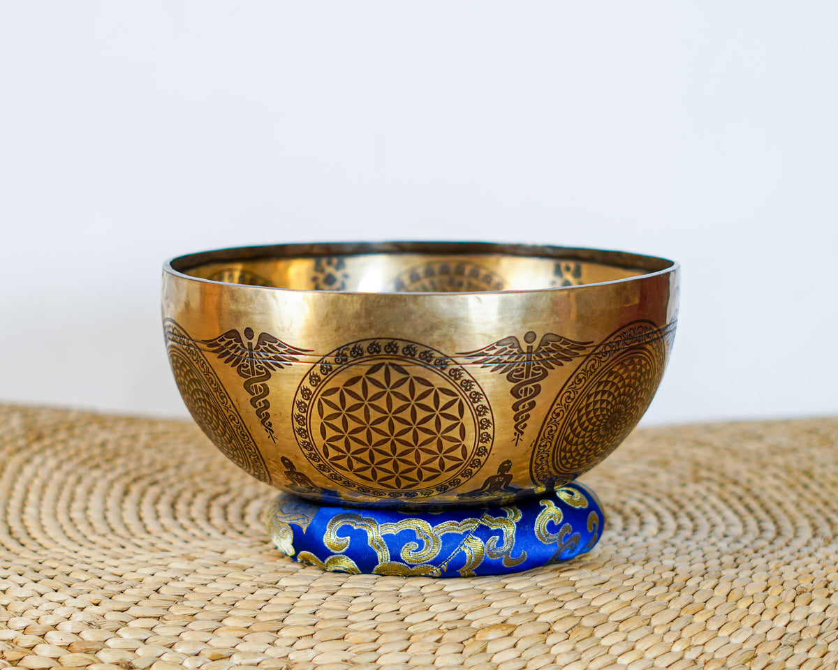 Golden Zambala singing bowl displayed on a blue brocade cushion, showcasing its engraved exterior and traditional design.