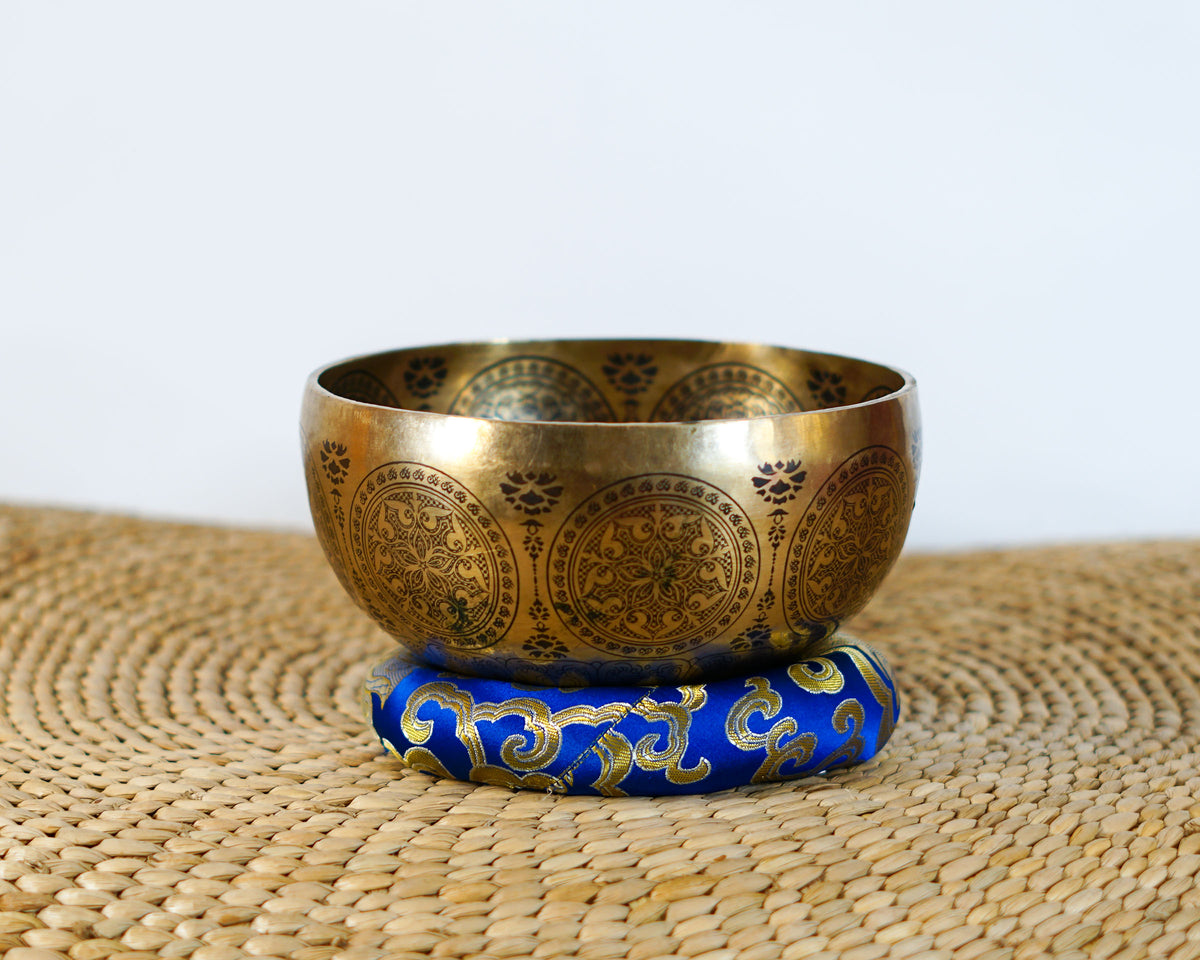 Golden Mahakala singing bowl resting on a blue brocade cushion, showing its engraved exterior and traditional ornamental details.