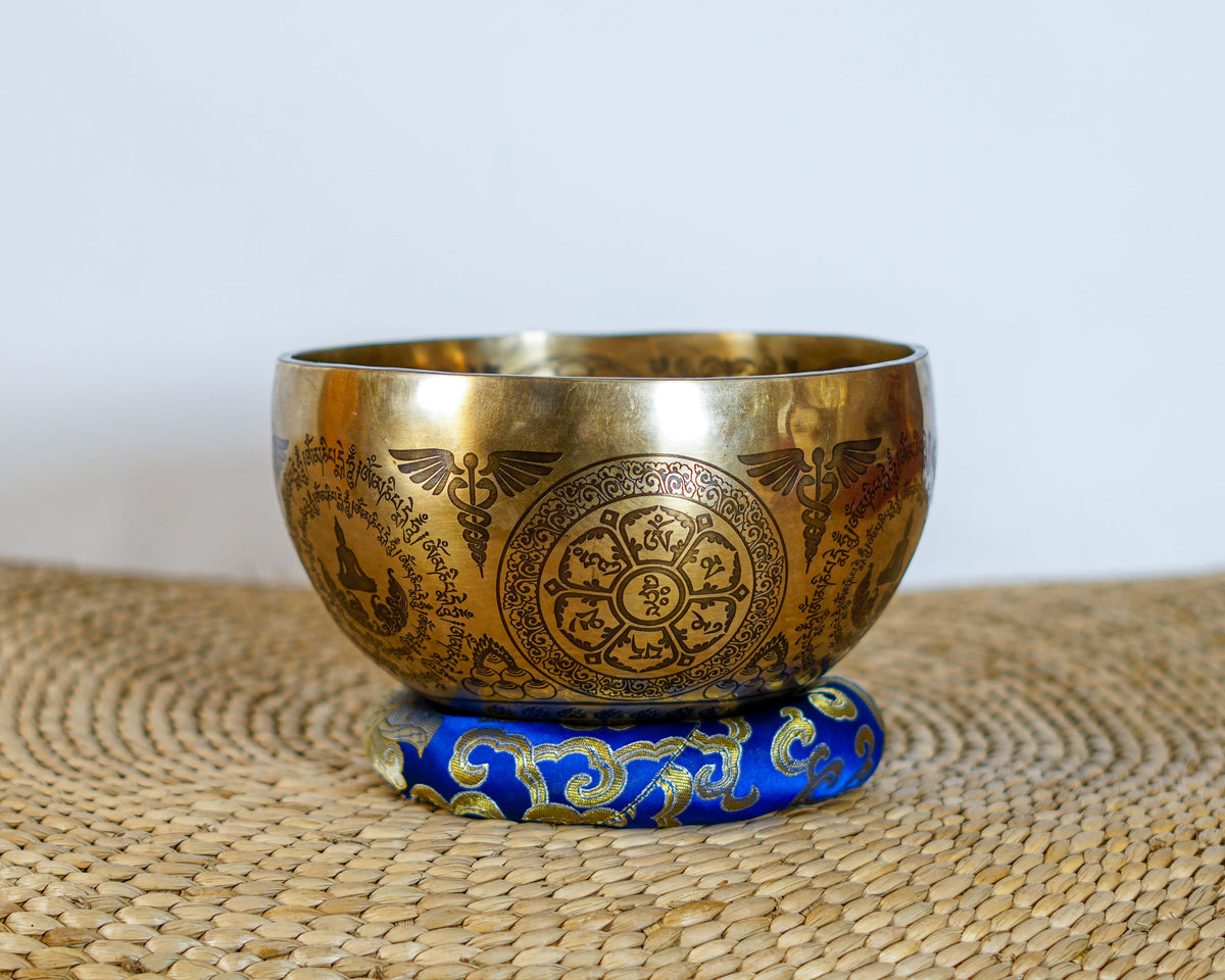 Golden Tree of Life singing bowl featuring intricate Tibetan inspired engravings on the exterior, displayed on a blue brocade cushion