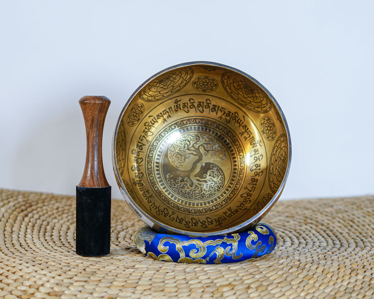 Golden Tree of Life singing bowl featuring intricate Tibetan inspired engravings on the exterior, displayed on a blue brocade cushion