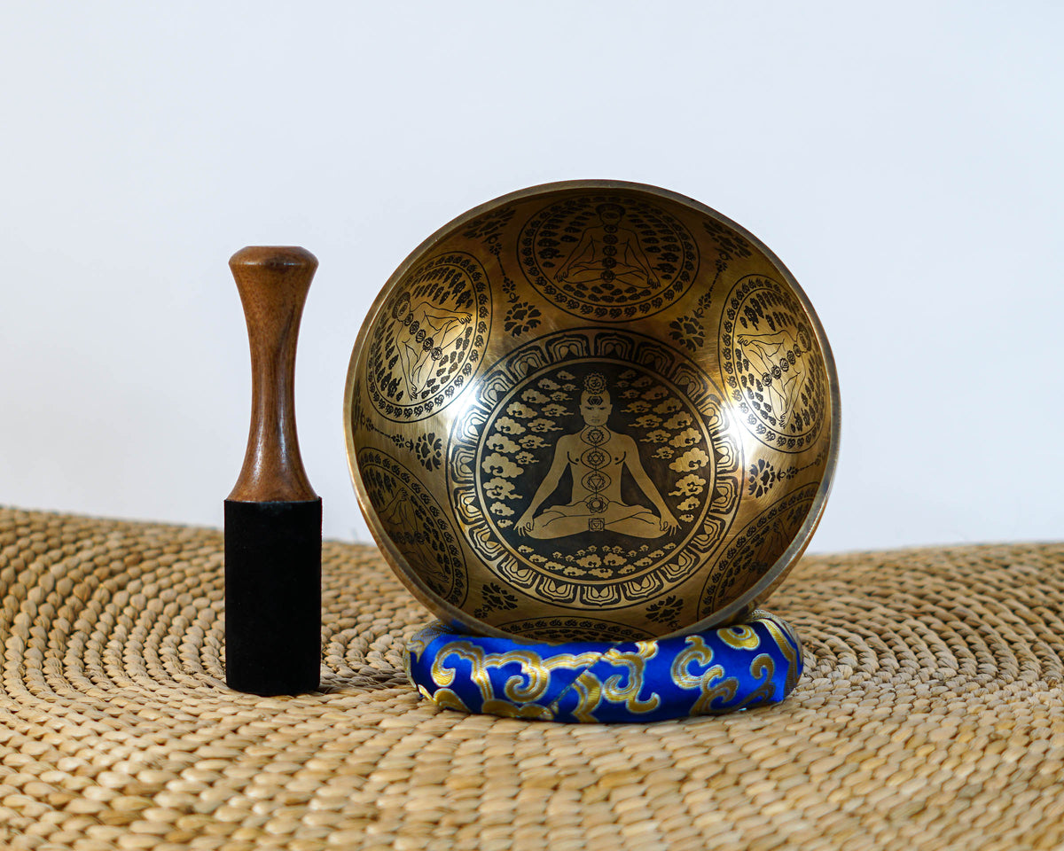 Seven Chakra singing bowl featuring an engraved meditating figure with chakra symbols inside a golden tone metal bowl.