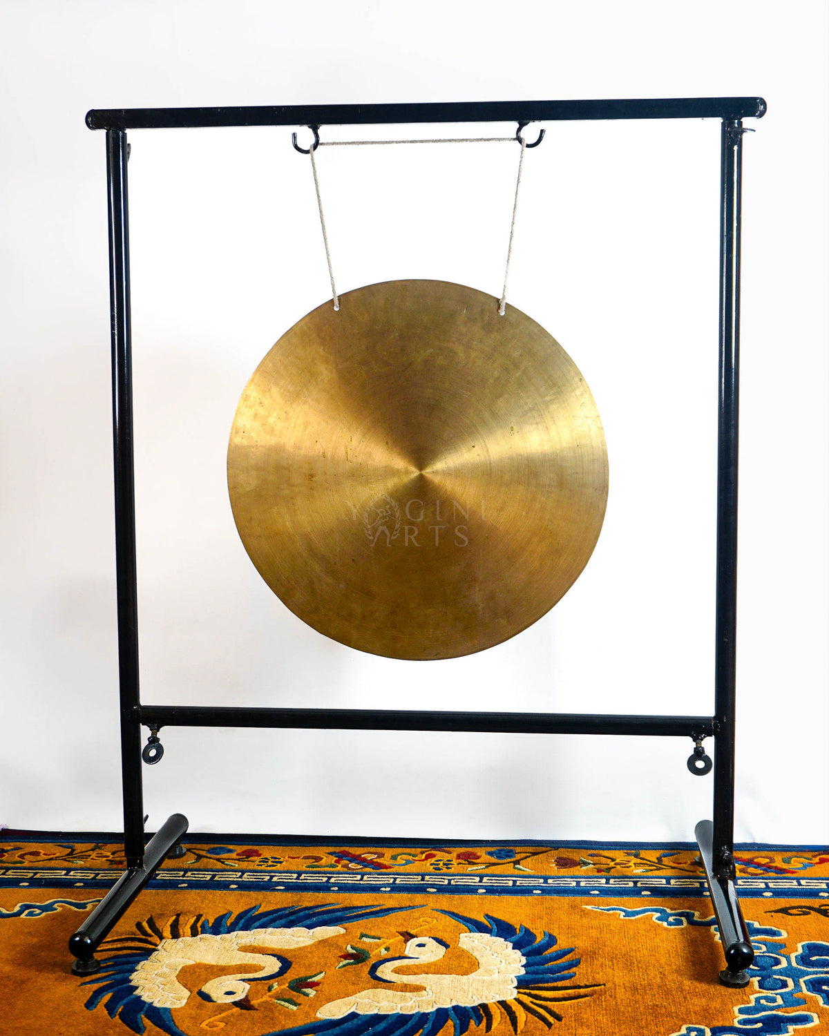 Handmade Tibetan-style gong with antique gold metallic finish suspended from a black metal stand on a colorful Himalayan-inspired rug.