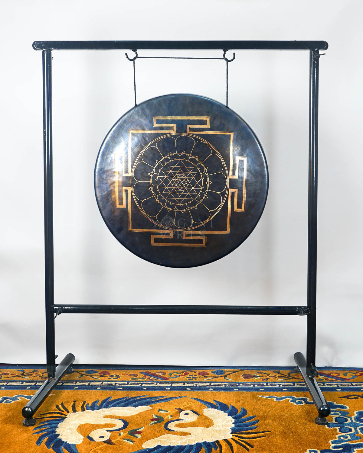 Handmade dark Tibetan-style gong with gold Sri Yantra-inspired mandala design suspended from a black metal stand.