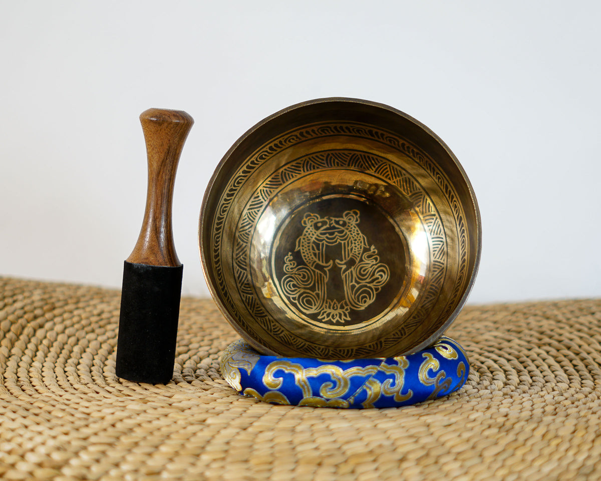 Handmade Tibetan singing bowl with Tibetan script engraved across its dark bronze exterior and gold rim.