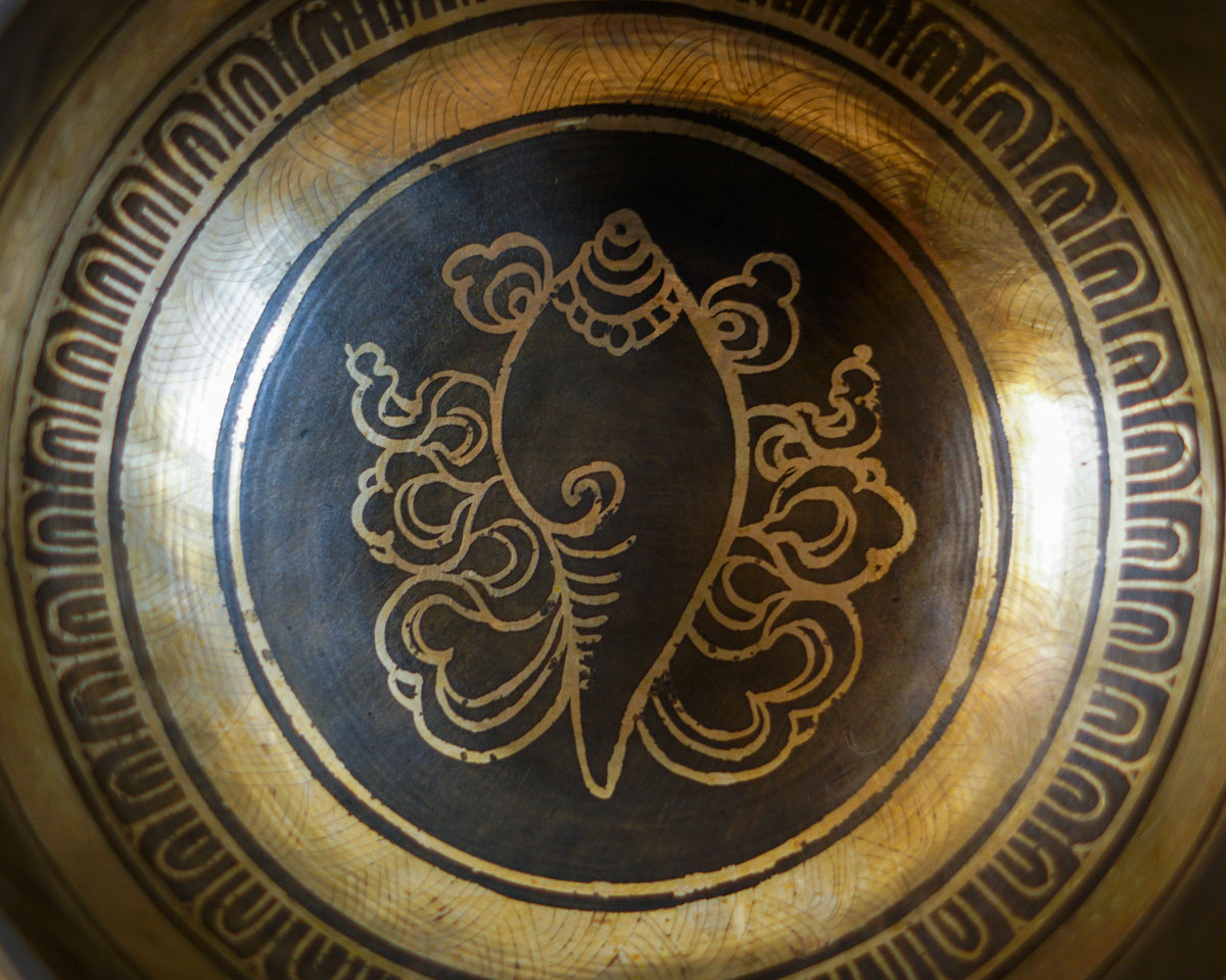 Close up of the conch shell symbol engraved inside an antique gold and dark bronze Tibetan singing bowl.