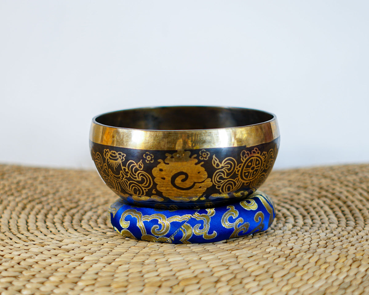 Buddha Eye singing bowl displaying engraved Wisdom Eyes inside the bowl with a wooden mallet and blue brocade cushion.