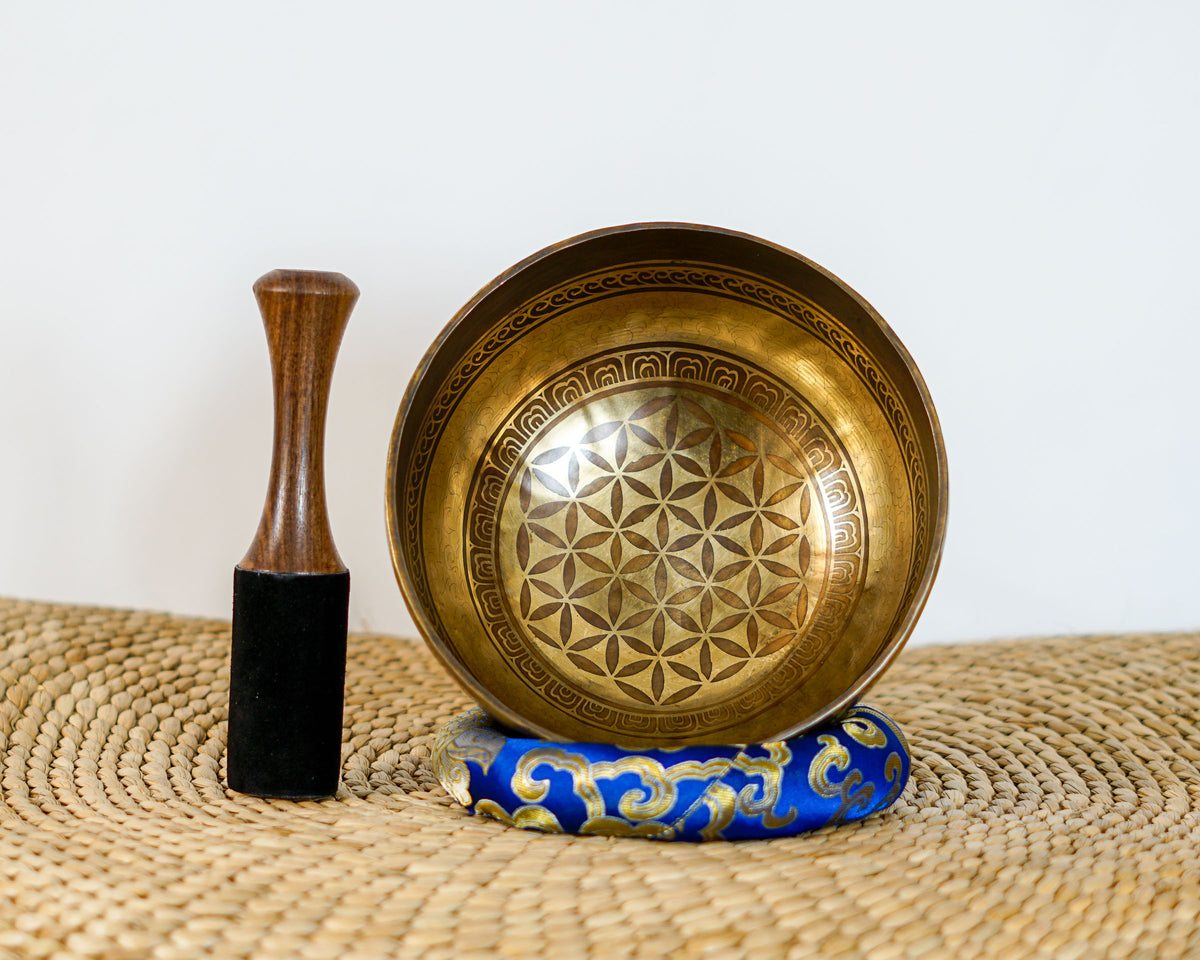 Tibetan singing bowl displaying the Flower of Life pattern inside, with a wooden mallet and blue brocade cushion.