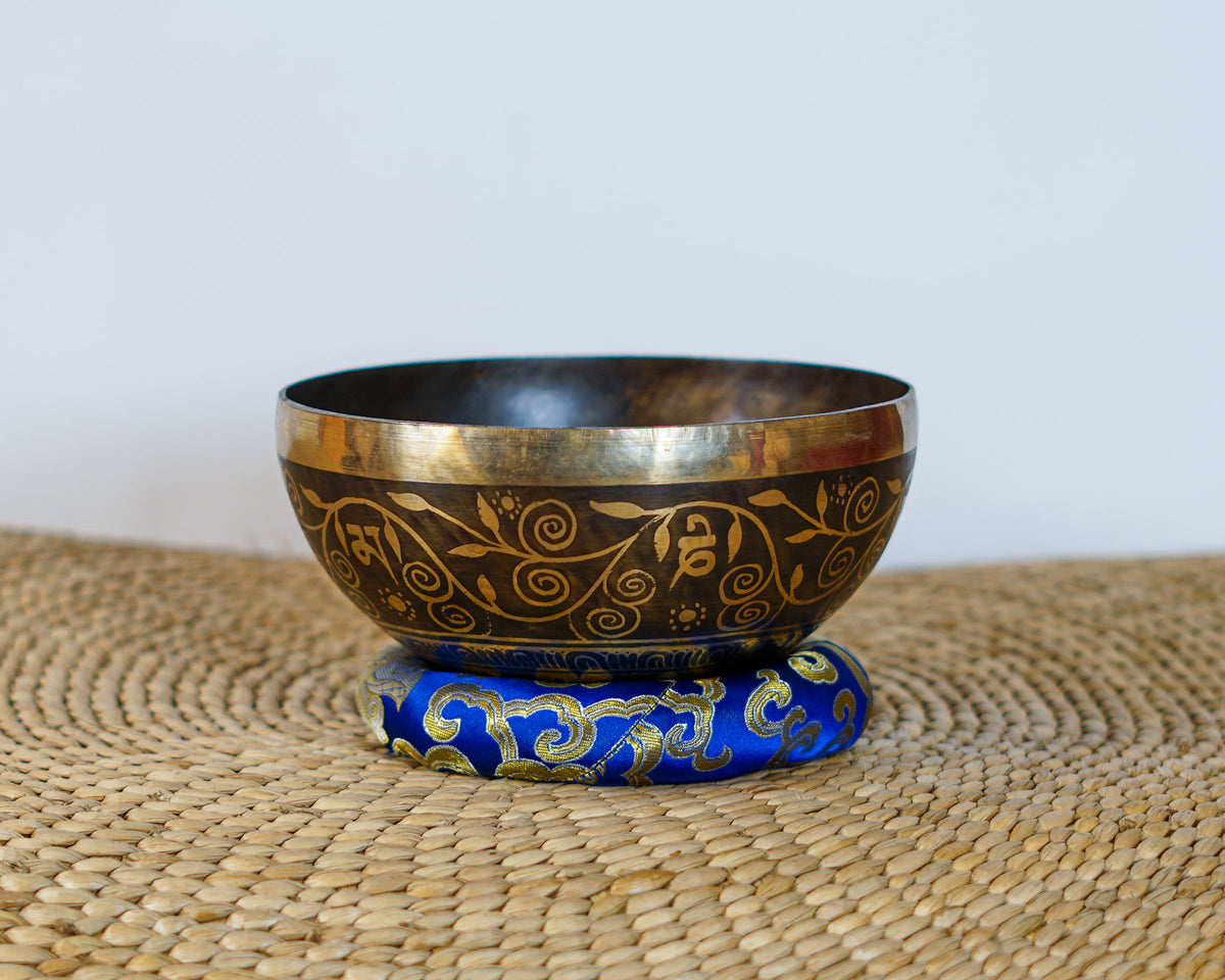 Handmade style Tree of Life singing bowl with golden decorative vine engravings on a blue brocade cushion.