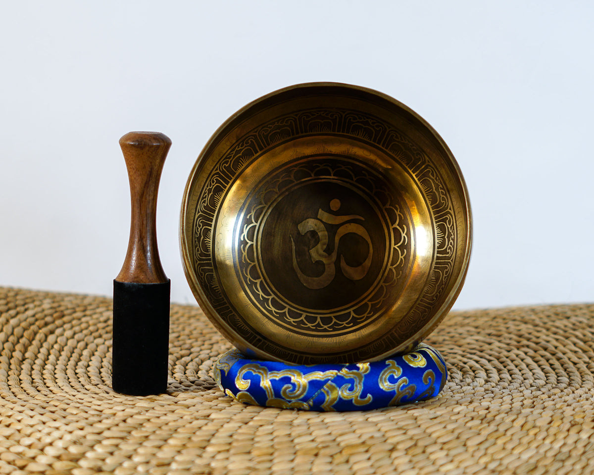 Hindu Om singing bowl displayed upright with a wooden mallet and blue brocade cushion, showing the engraved Om symbol inside.