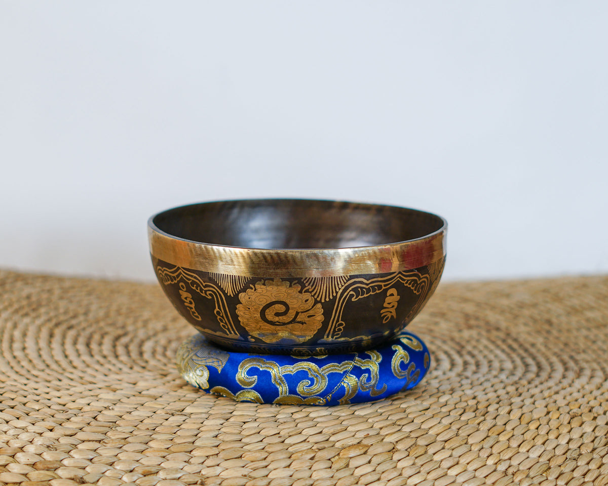 Hindu Om singing bowl with antique gold and dark engraved exterior displayed on a blue brocade cushion.