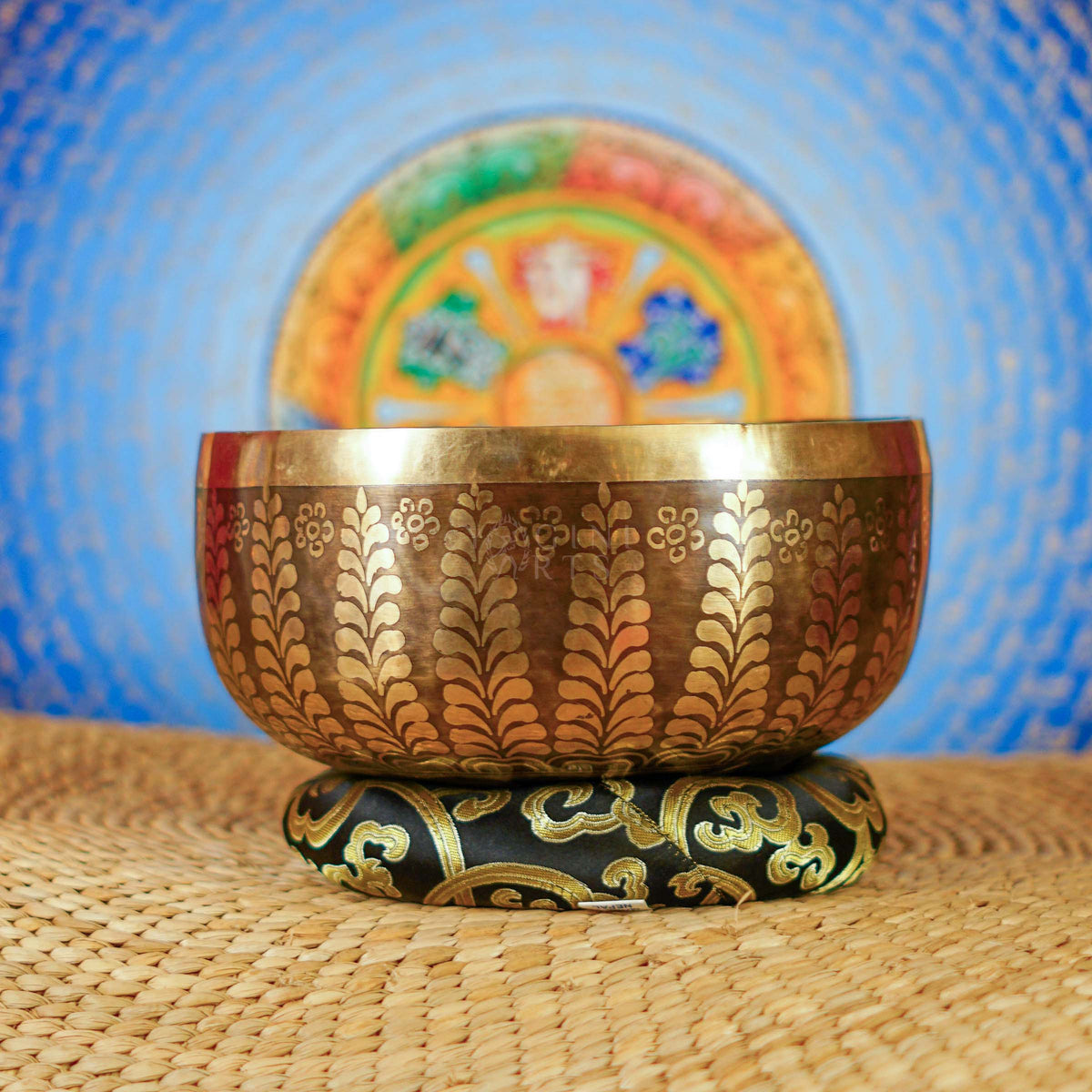 Handcrafted Nepal singing bowl with meditating figure and chakra engraving, floral design, bronze finish, cushion and wooden striker.