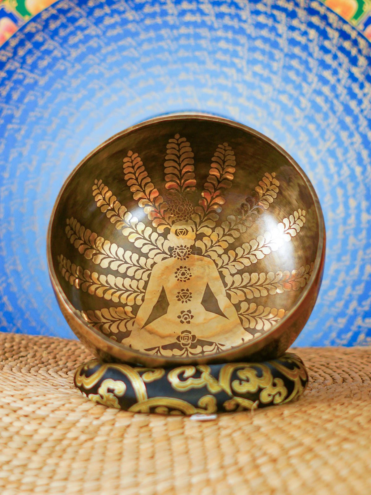 Handcrafted Nepal singing bowl with meditating figure and chakra engraving, floral design, bronze finish, cushion and wooden striker.