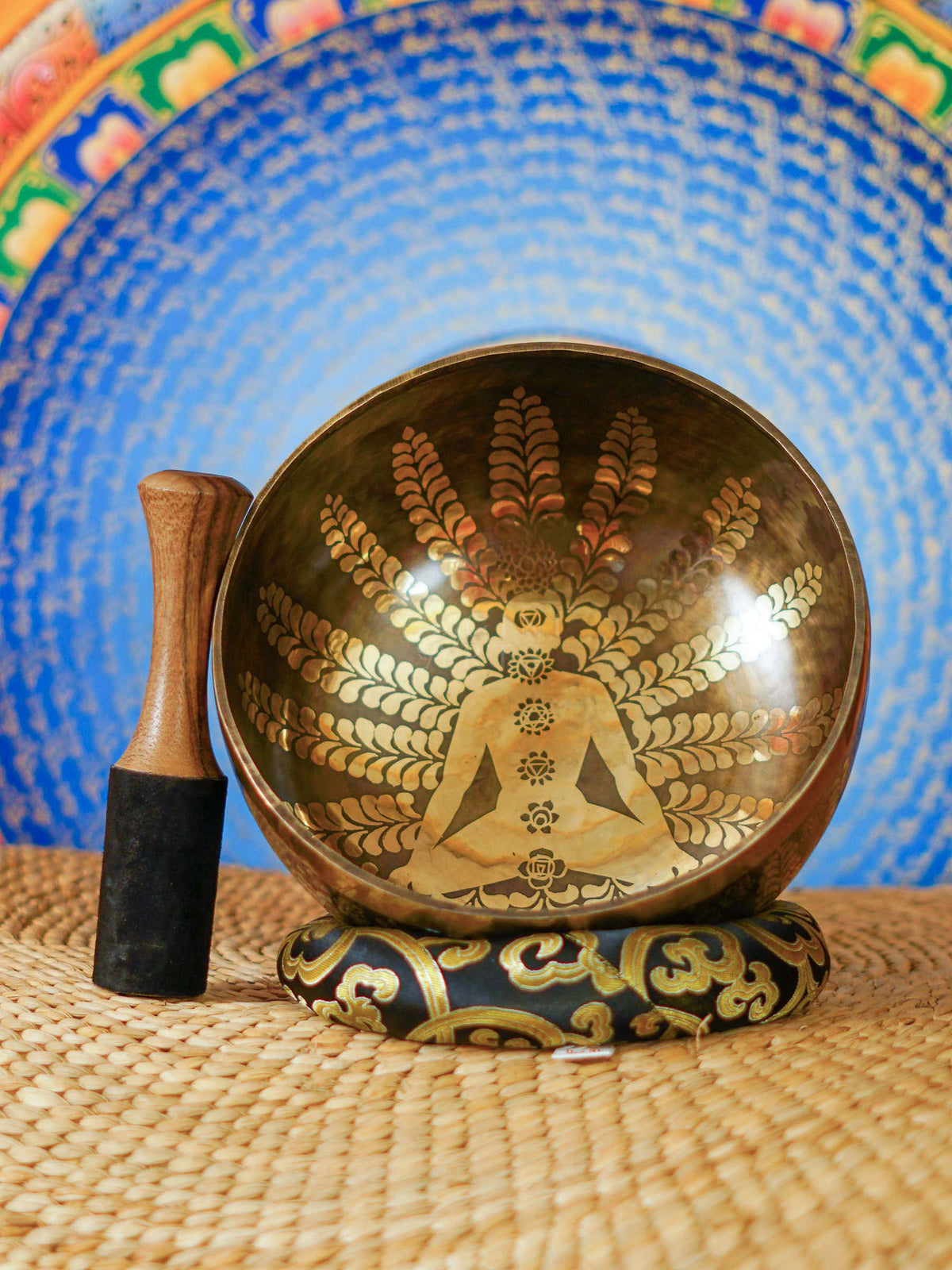 Handcrafted Nepal singing bowl with meditating figure and chakra engraving, floral design, bronze finish, cushion and wooden striker.