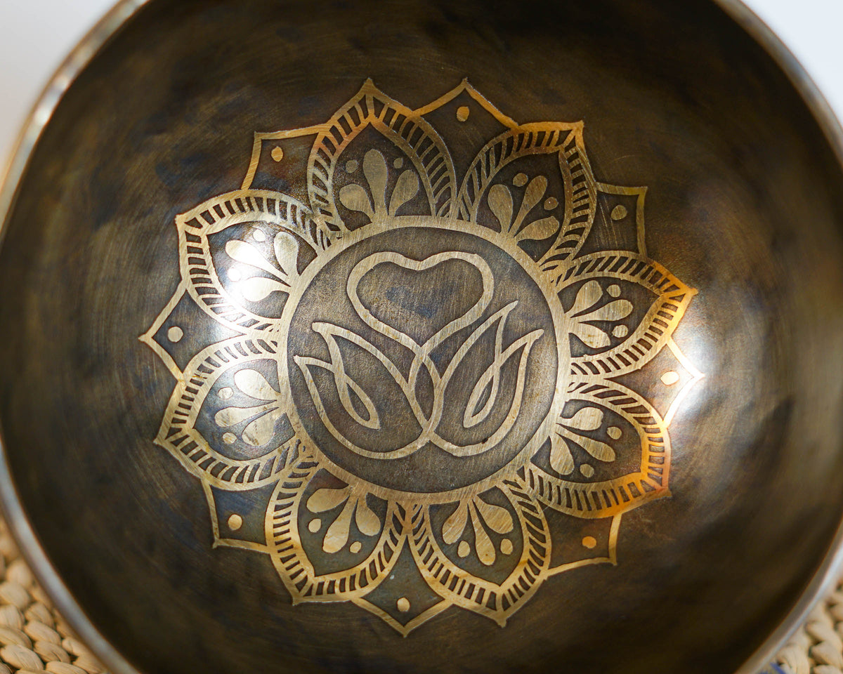 Close up of a golden Swan Symbol of Life motif with a heart and lotus inspired mandala engraved inside a dark antique Tibetan singing bowl.