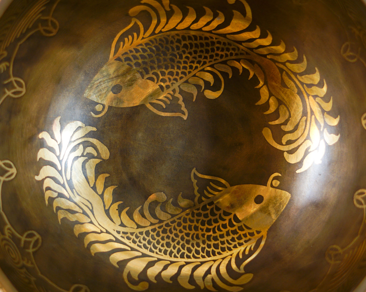 Close up of the golden twin fish pair intricately engraved inside a dark antique bronze Tibetan singing bowl.