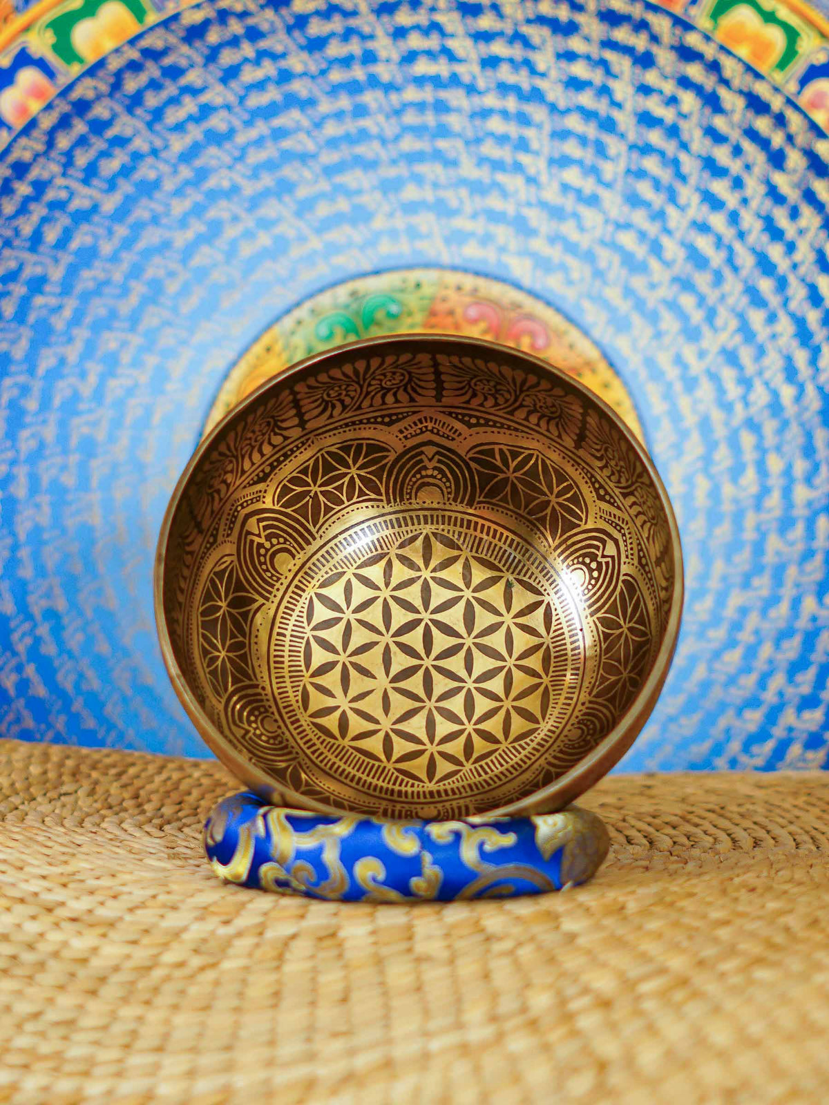 Handcrafted Flower of Life singing bowl from Nepal with sacred geometry engraving, Tibetan-style motifs, bronze-gold finish and blue cushion.