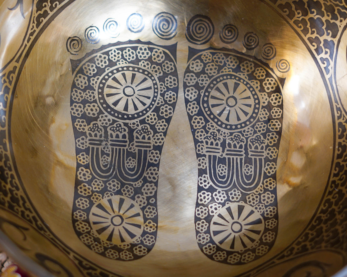 Close up of sacred Buddha footprints engraved inside a golden Tibetan singing bowl with intricate floral details.