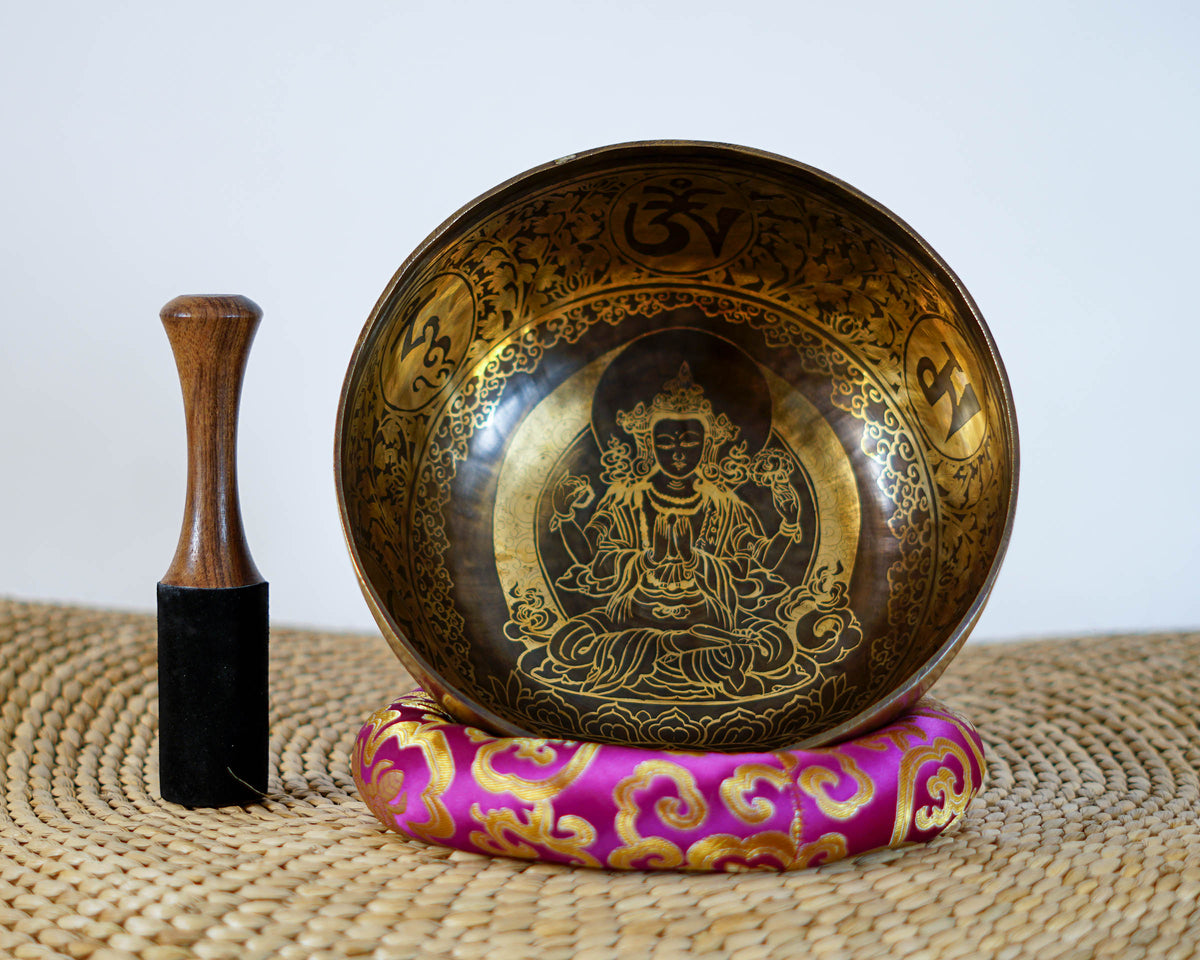 Chengresi Tibetan singing bowl with engraved floral patterns shown upright on a pink cushion beside a wooden striker.