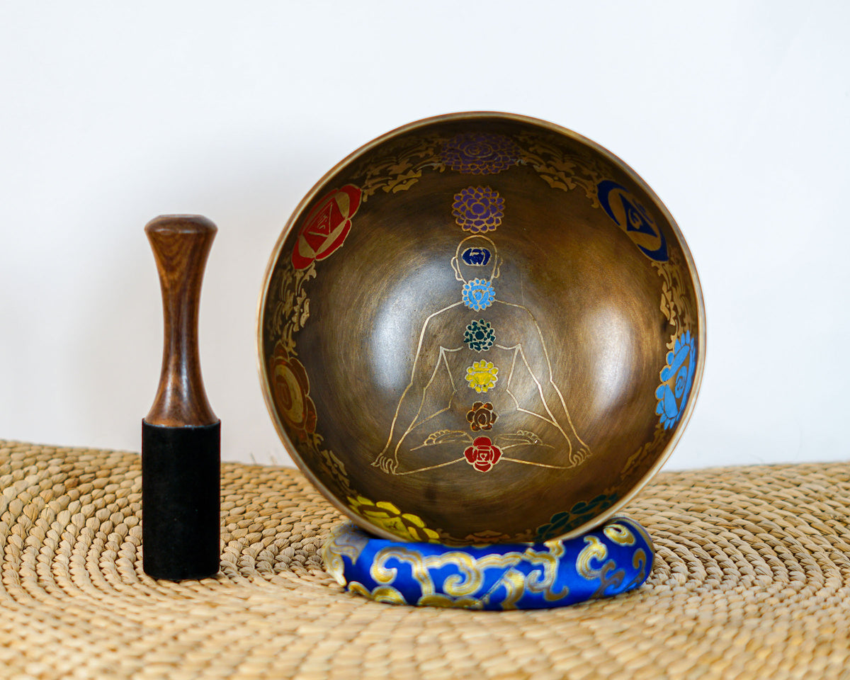 Top-angled view of a 7 chakra meditating yogi Tibetan singing bowl on a blue cushion next to a wooden striker mallet.