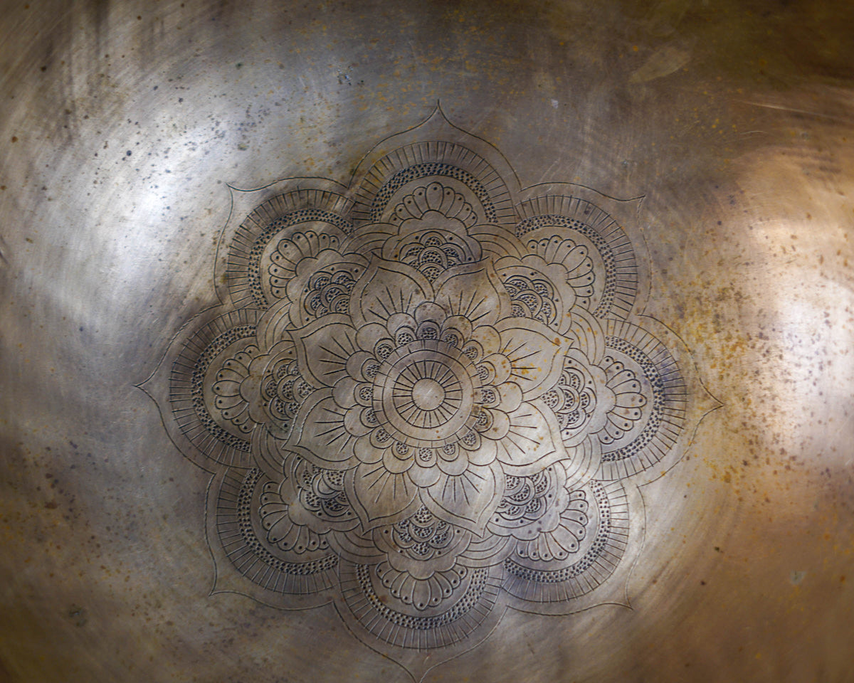 Close up of an intricate lotus flower mandala finely engraved inside a warm golden bronze hand-hammered singing bowl.
