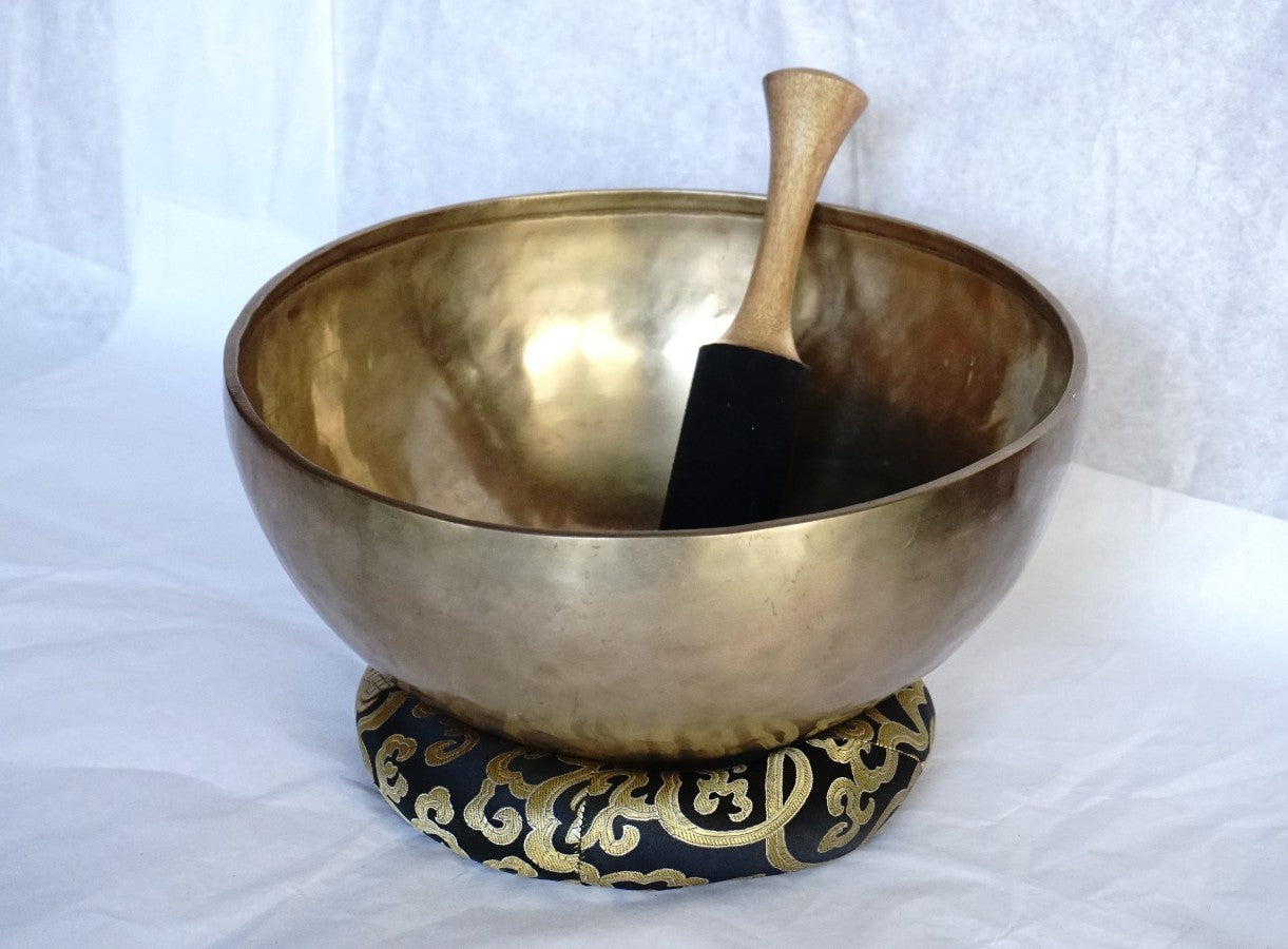 Handcrafted Tibetan brass singing bowl with wooden striker on brocade cushion