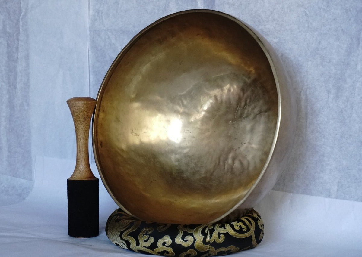 Handcrafted Tibetan brass singing bowl with wooden striker on brocade cushion