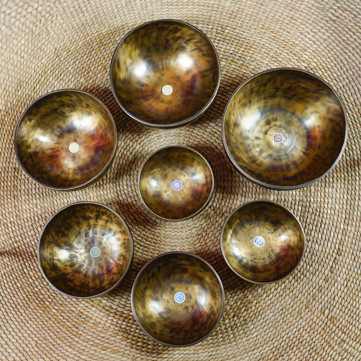 Seven handcrafted chakra singing bowls arranged together, showing different sizes, warm antique metallic finishes and individual chakra symbols.