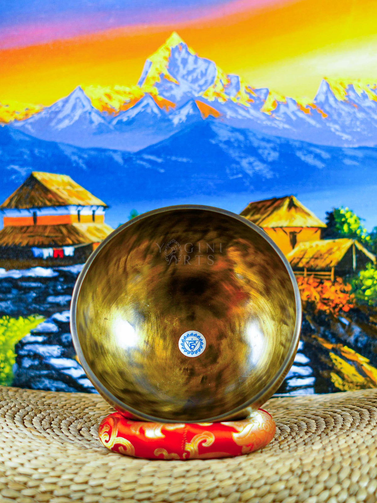Front view of a chakra singing bowl displaying the Om symbol inside a warm bronze-gold metal bowl on a red cushion.