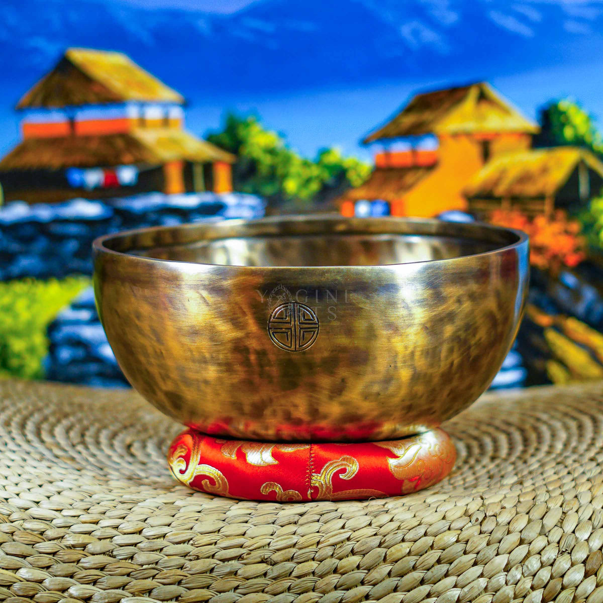 Side view of a handcrafted Himalayan singing bowl with warm bronze-gold finish, engraved Tibetan-style inscription and red decorative cushion.