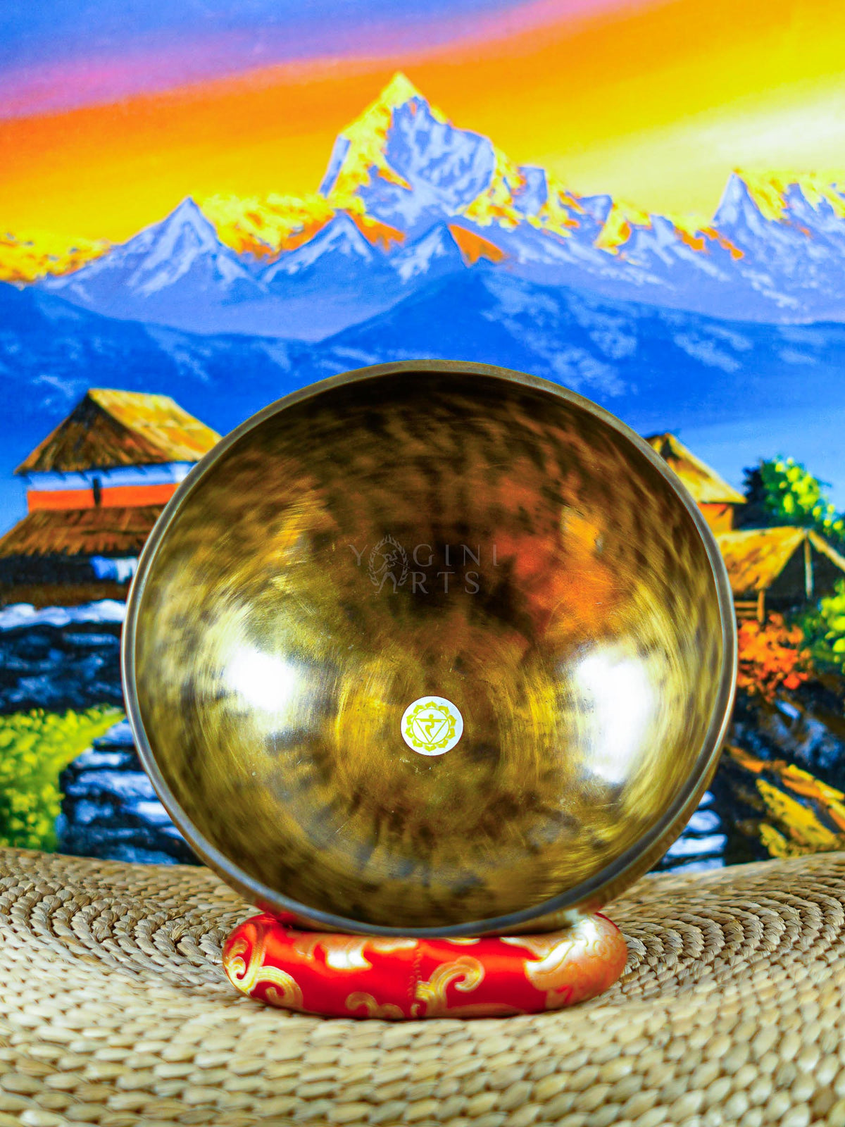 Front view of a chakra singing bowl displaying the Om symbol inside a warm bronze-gold metal bowl on a red cushion.
